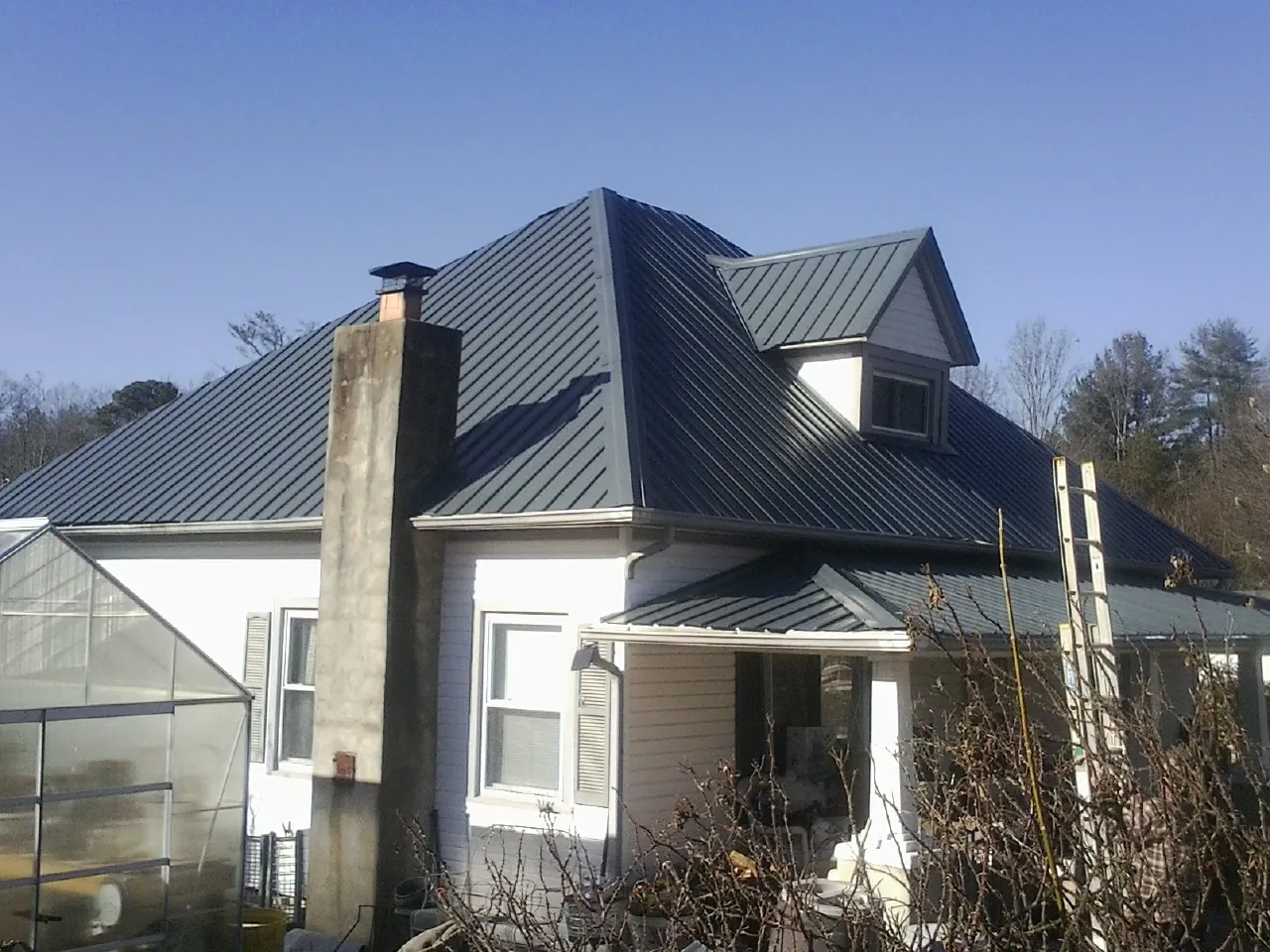 Dark blue standing seam metal roof on a white farmhouse with dormer — Slate & Tile Roof Repair by Roofing Brothers in Vaughn