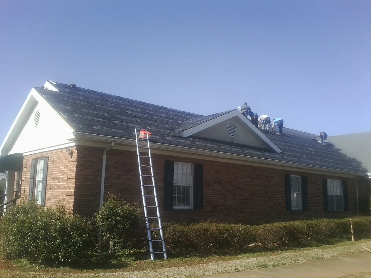 Crew tearing shingles off a brick ranch roof with a ladder set — Emergency Roof Repair work by our crew in Vaughn