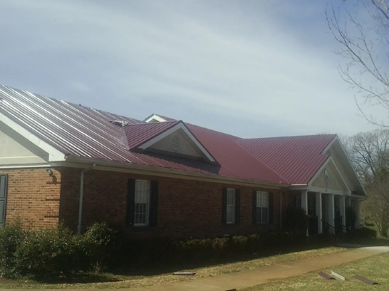 Red metal roof with gabled entries on a long brick building, from a Hail Damage Roof Repair job in Vaughn