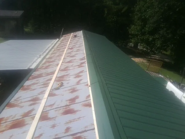 Old rusted panels beside newly installed green metal roofing — Wind Damage Roof Repair by Roofing Brothers in Vaughn
