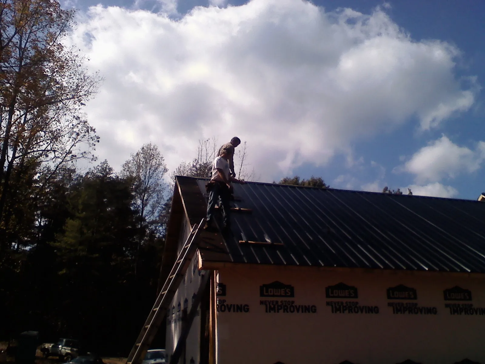 Roofer fastening dark metal panels high against a cloudy sky, from a Roof Inspection job in Vaughn